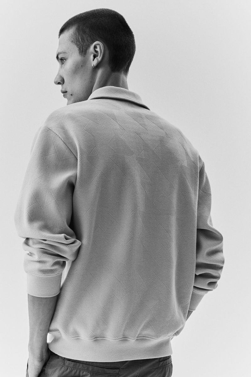 Close-up portrait of a male model wearing a collared textured top against a plain light studio background.