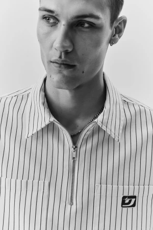 Close-up monochrome portrait of a young man wearing a striped zip-up collared shirt against a white background for H&M.