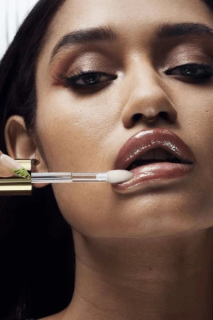 Close-up shot of a young adult female applying clear lip gloss with an applicator, showcasing glossy lips, makeup and nail art details.