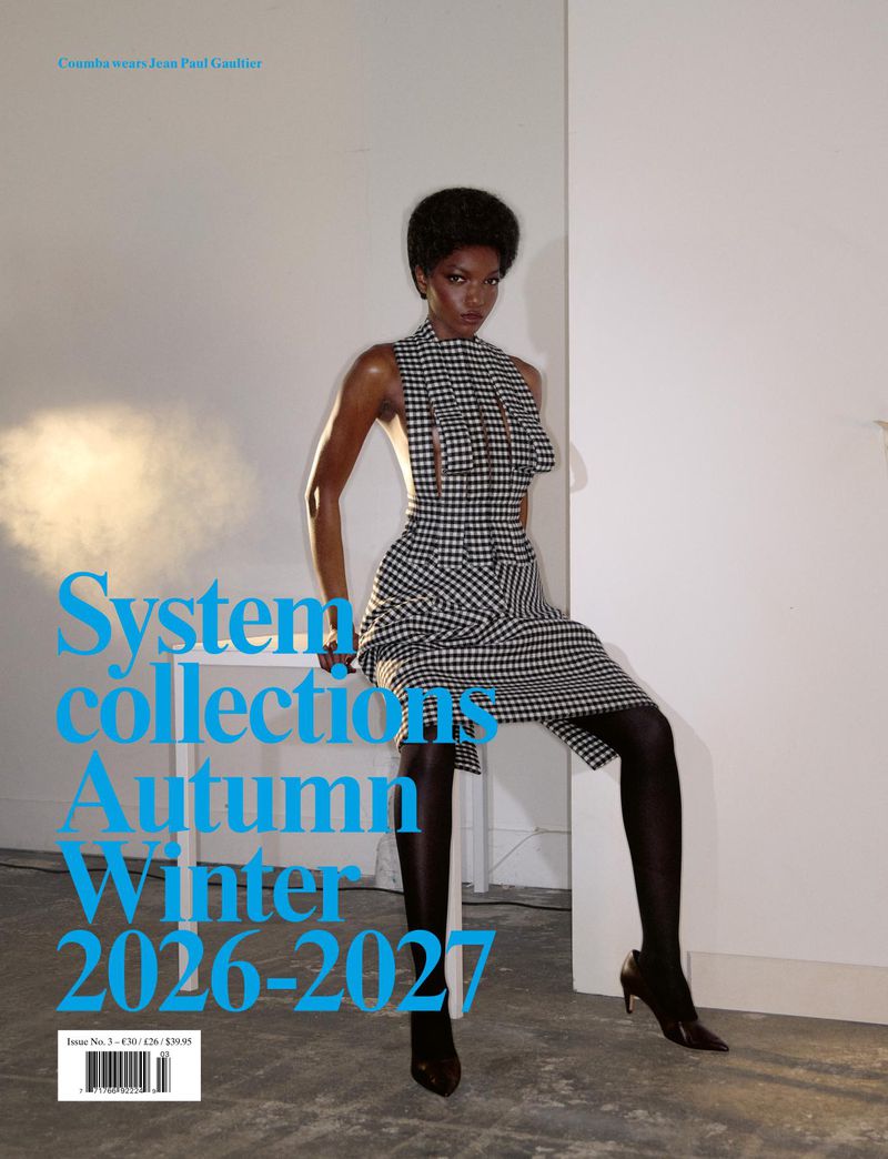Model wearing a black and white houndstooth dress and dark tights sitting on a white table in an interior studio space