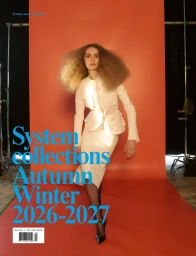 Model in white jacket and skirt standing in front of an orange seamless background with studio lighting.