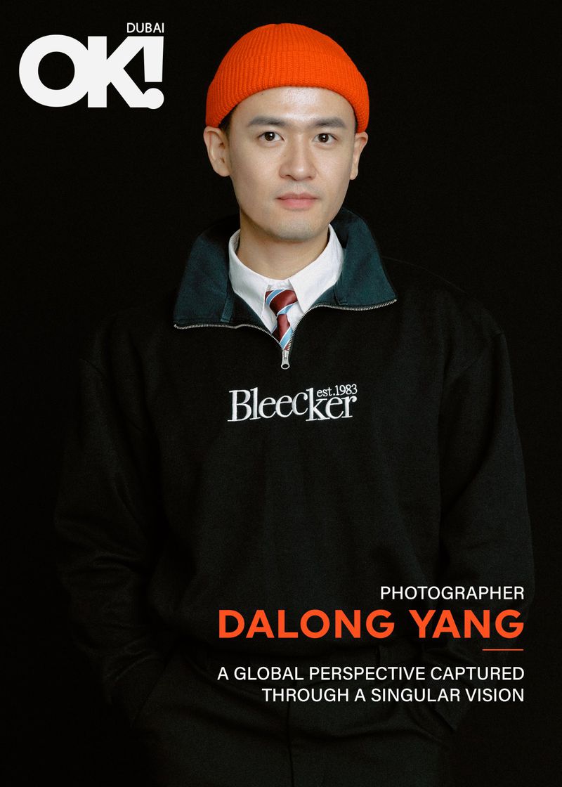 OK! Dubai cover featuring a portrait of photographer Dalong Yang wearing a dark sweatshirt and an orange beanie against a black backdrop.