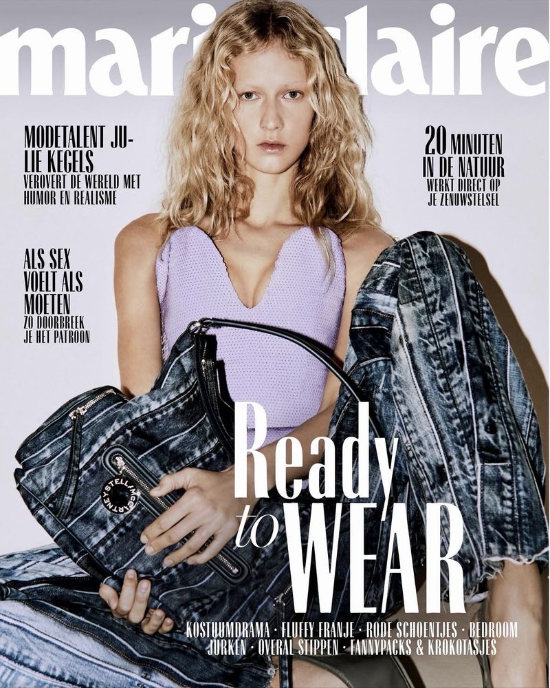 Magazine cover featuring a blonde model in a lavender top and denim trousers holding a dark bag against a white backdrop.