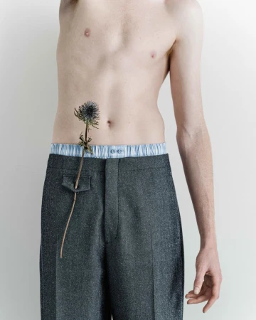 Torso shot of shirtless adult male wearing grey trousers with a thistle on his stomach in a photo studio against a white backdrop.