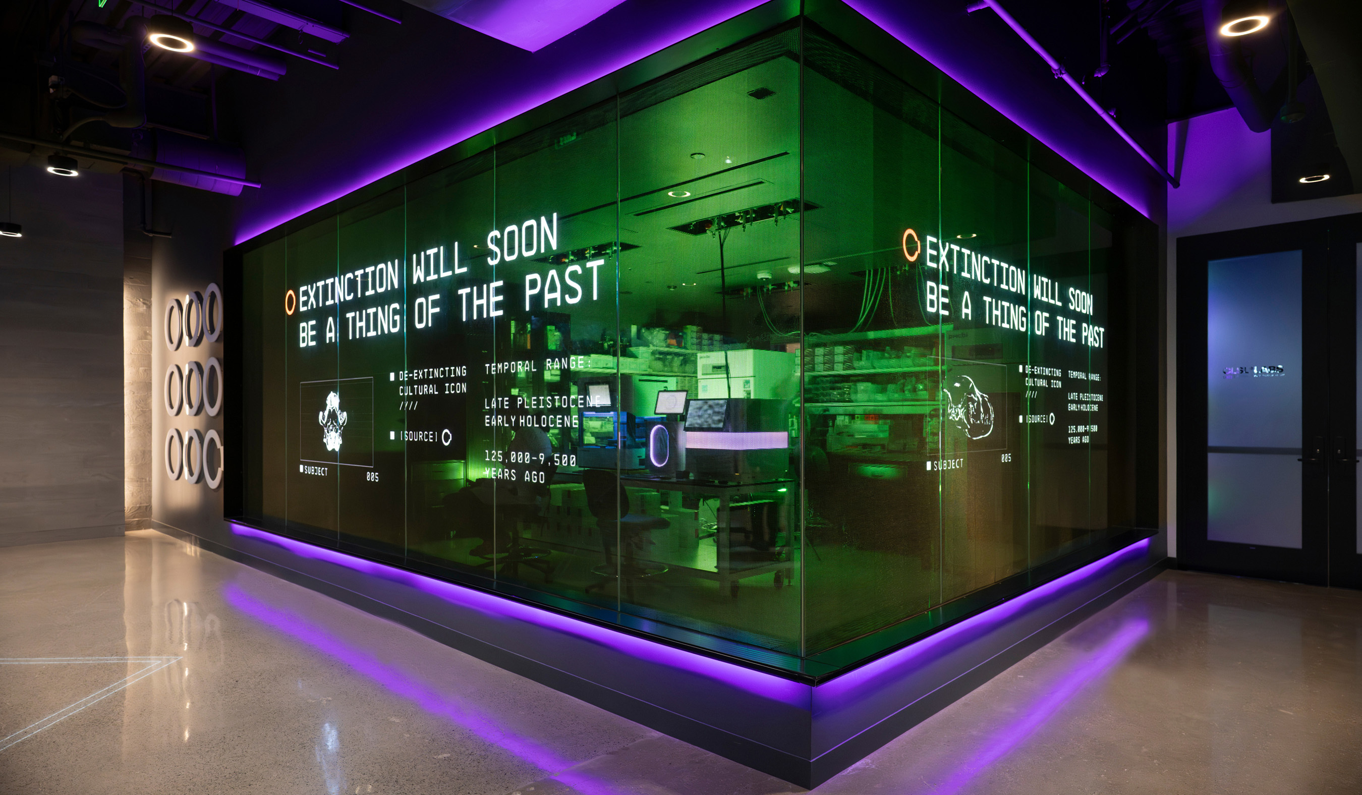 Illuminated glass laboratory room with green interior light and purple floor LEDs displaying extinction text for Colossal Dallas HQ