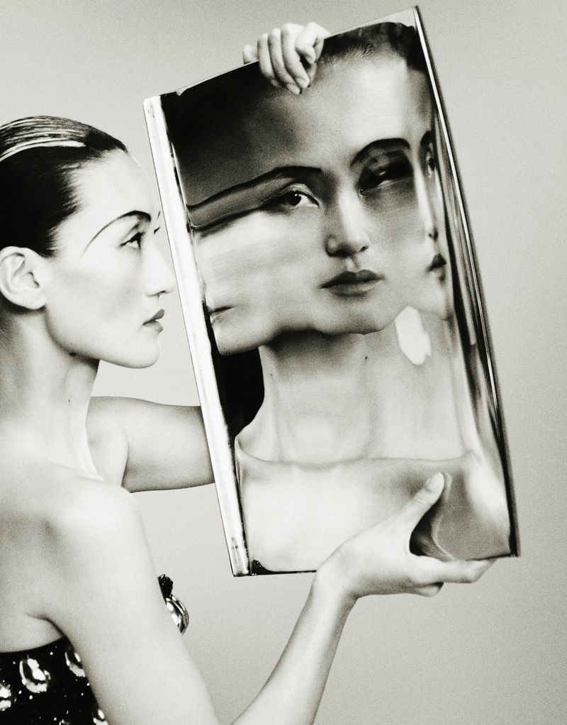 Monochrome fashion shot of an Asian woman in elegant dress holding a framed picture of her face, creating a multi-face portrait.