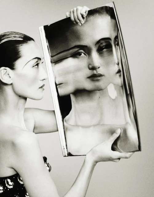 Monochrome fashion shot of an Asian woman in elegant dress holding a framed picture of her face, creating a multi-face portrait.