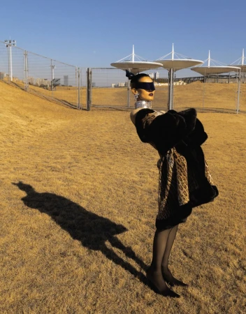 Fashionable mannequin in black and animal-print dress, black hosiery, and heels stands in a grassy field against a blue sky backdrop.