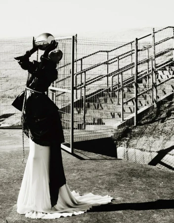 Fashion photography of a person in a black jacket and long white skirt holding a reflective ball in an outdoor urban setting.