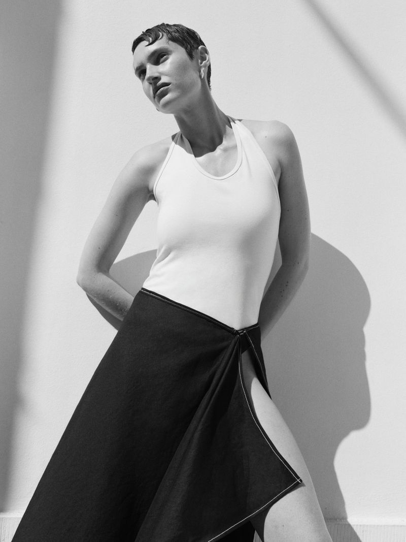 Monochrome fashion portrait of a short-haired woman wearing a white halter top and dark skirt against a bright sunlit wall