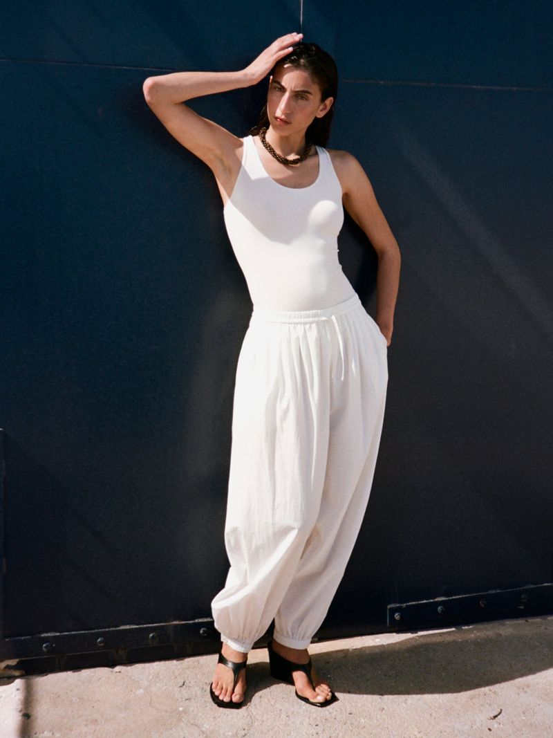 Model in white tank top and trousers leaning against a dark wall for the Arket SS26 campaign