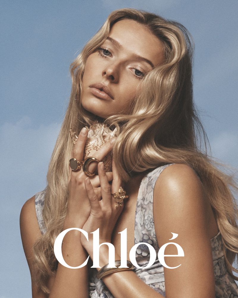 Model with long blonde hair holding a seashell against a clear blue sky background for Chloé
