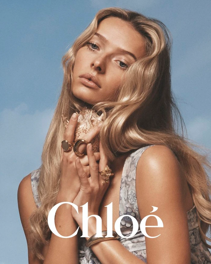 Model with long blonde hair holding a seashell against a clear blue sky background for Chloé