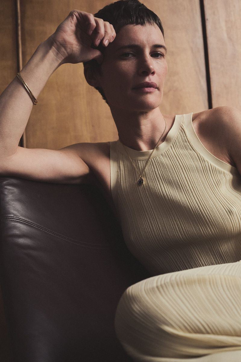 Woman in cream ribbed tank top seated on a dark leather chair against wood paneling
