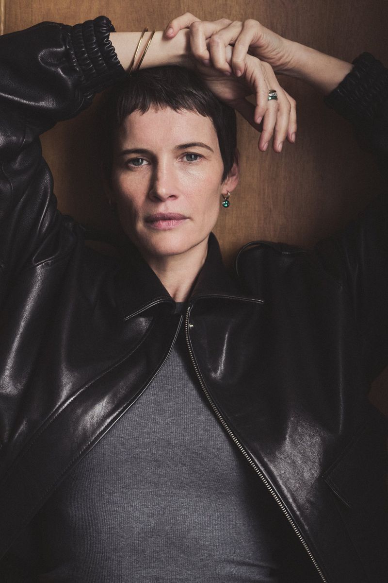 Portrait of a woman with short dark hair wearing a black leather jacket against a wooden wall