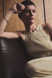 Woman in cream ribbed tank top seated on a dark leather chair against wood paneling