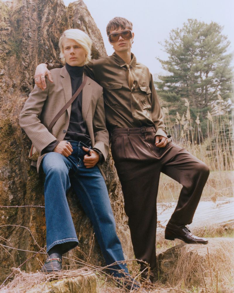 Two male models posing outdoors near a large rock formation and trees for Numéro New York editorial