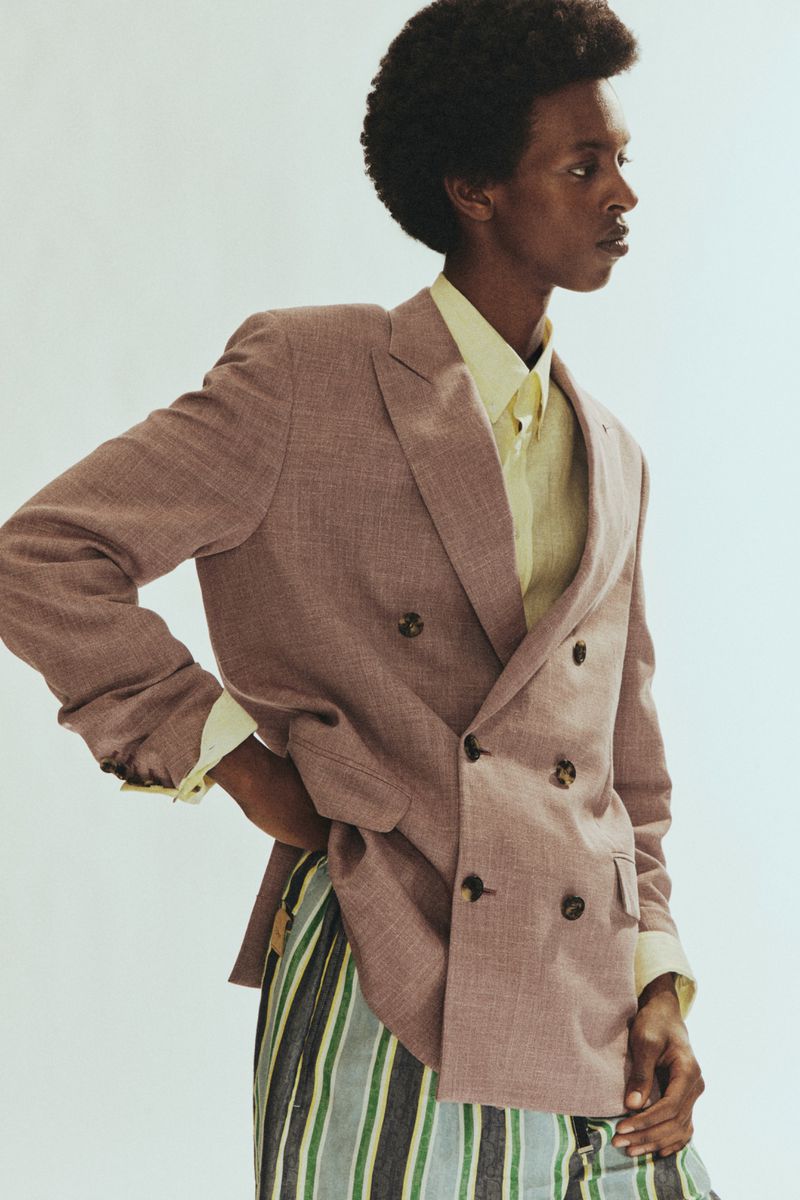 Model wearing a double-breasted brown blazer and striped trousers against a plain light background