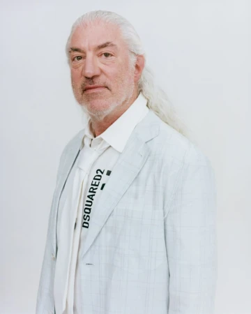 Portrait of an elderly man with long white hair and beard wearing a light blazer and white tie against a plain white background