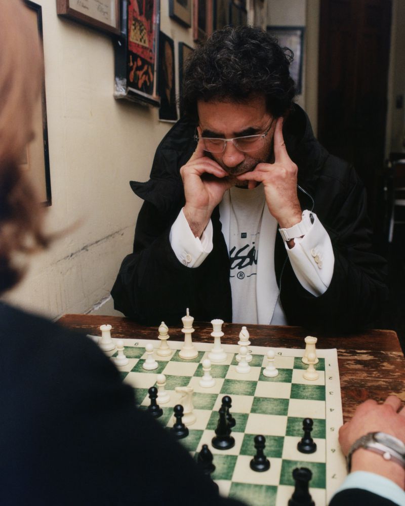 A man wearing glasses sitting across a wooden table playing a game of chess indoors.