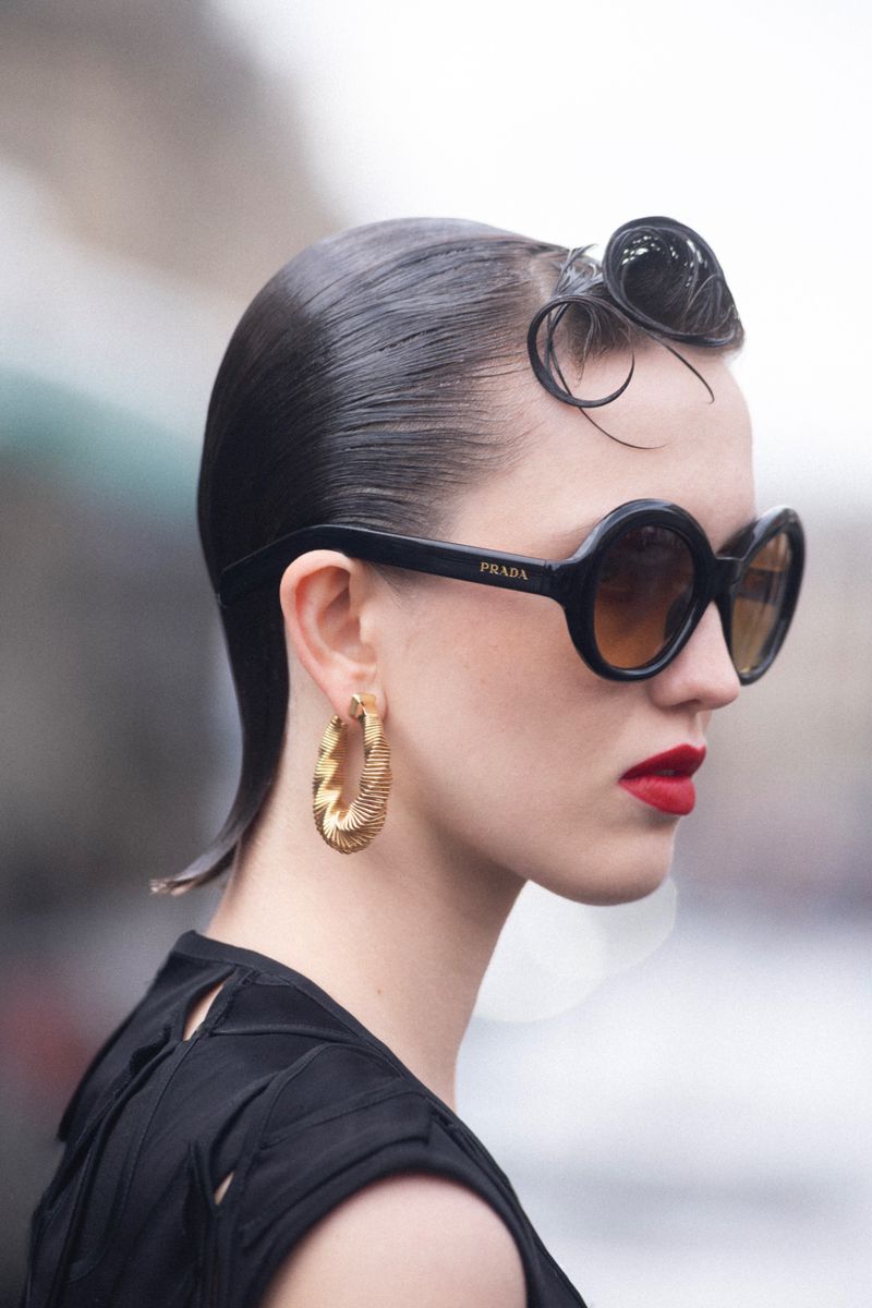 Profile portrait of a woman wearing round sunglasses, red lipstick, and a gold hoop earring for Elle Hungary.