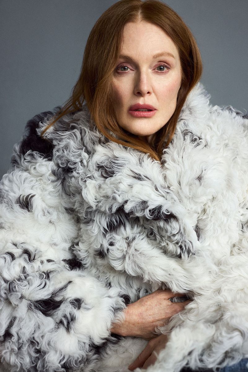 Julianne Moore wearing a textured white and black patterned fur coat against a solid grey studio background.