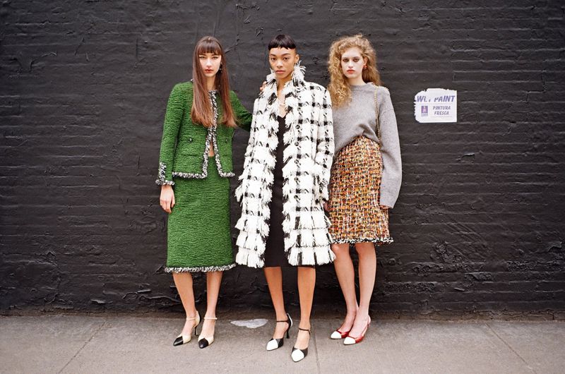 Three female models posing in textured skirts and coats against a dark painted brick wall for SCMP Style