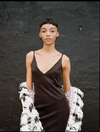 Model wearing a dark slip dress and textured monochrome jacket against a dark textured wall for SCMP Style.