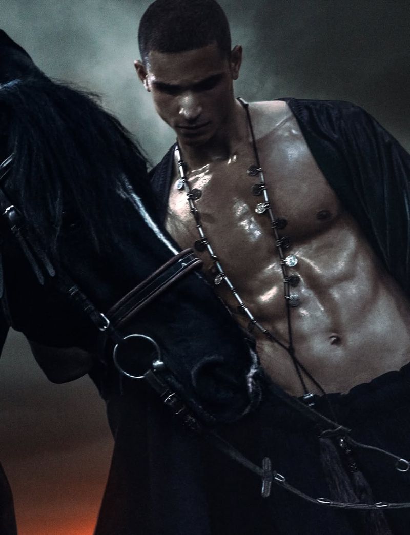Close-up portrait of a shirtless male model standing next to a black horse for Numero Netherlands editorial Wild Narcissus