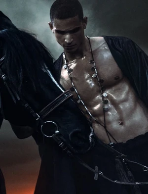 Close-up portrait of a shirtless male model standing next to a black horse for Numero Netherlands editorial Wild Narcissus
