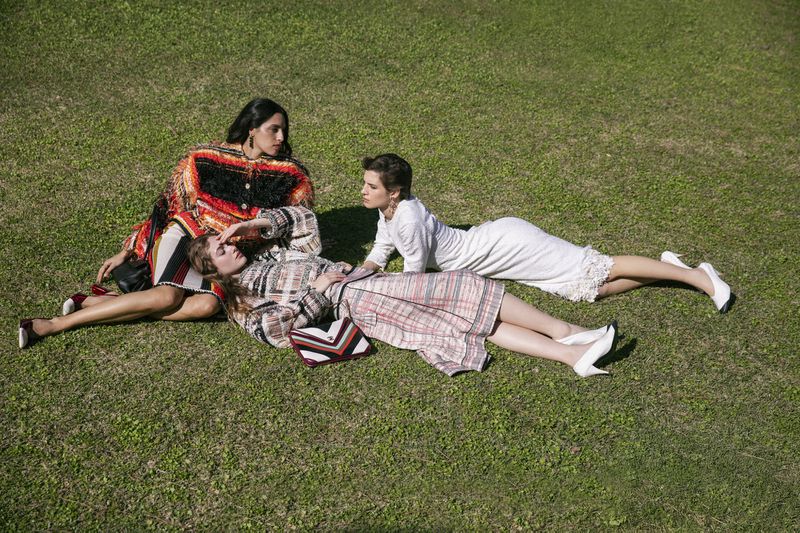 Three female models lounging on a green lawn wearing patterned tweed clothing and white heels for Marie Claire Greece.