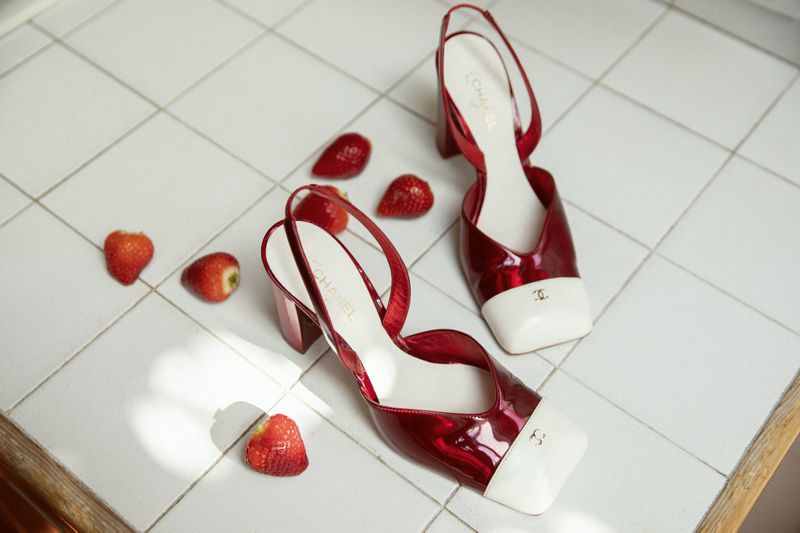 Glossy red and white slingback heels resting on white tiled floor alongside fresh sliced strawberries for Chanel special.