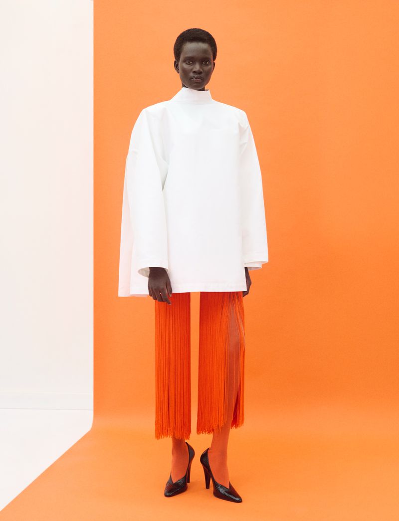 Model Aluel Keror in a white top and orange fringed trousers standing against an orange and white backdrop for Exit Magazine