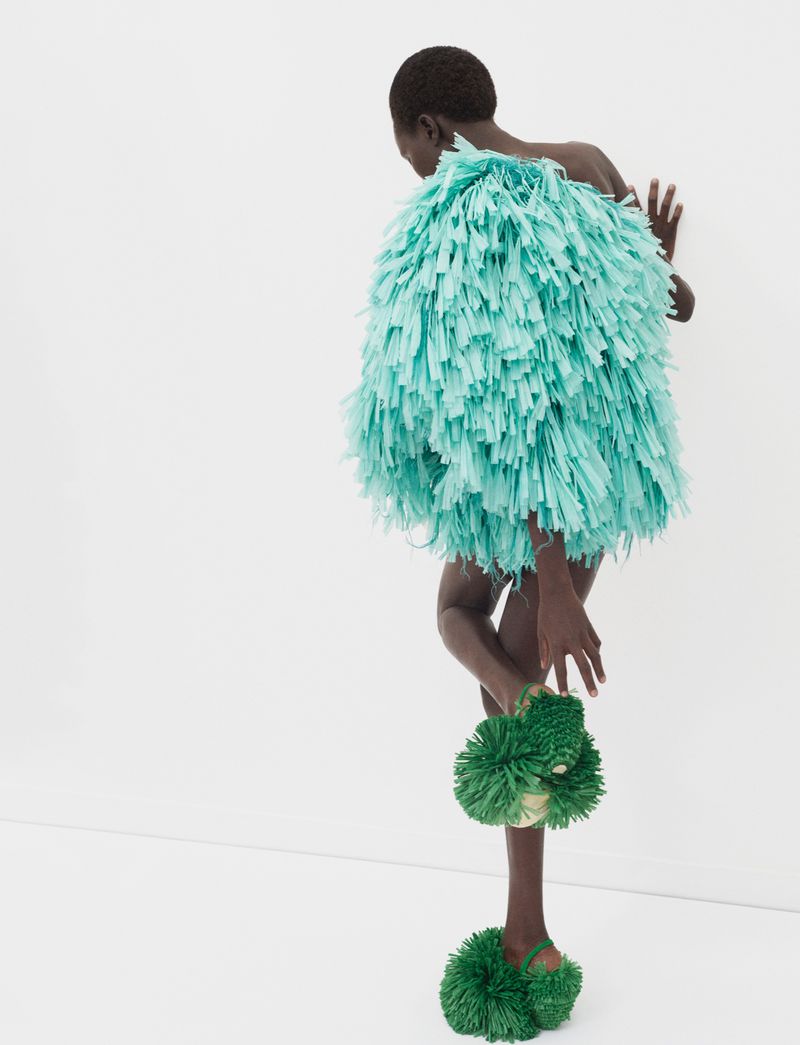 Model Aluel Keror wearing a textured mint fringe dress and green fuzzy shoes against a white backdrop