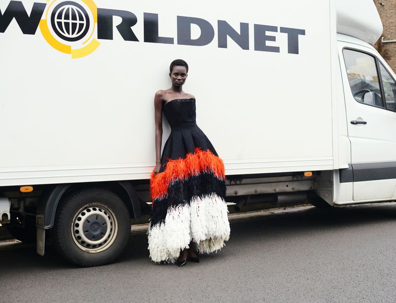 Model Aluel Keror in a tiered feathered gown leaning against a white Worldnet delivery truck for Exit Magazine