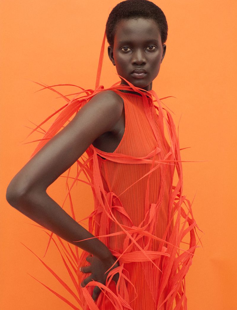 Model Aluel Keror wearing an orange fringed dress against a vibrant orange background for Exit Magazine