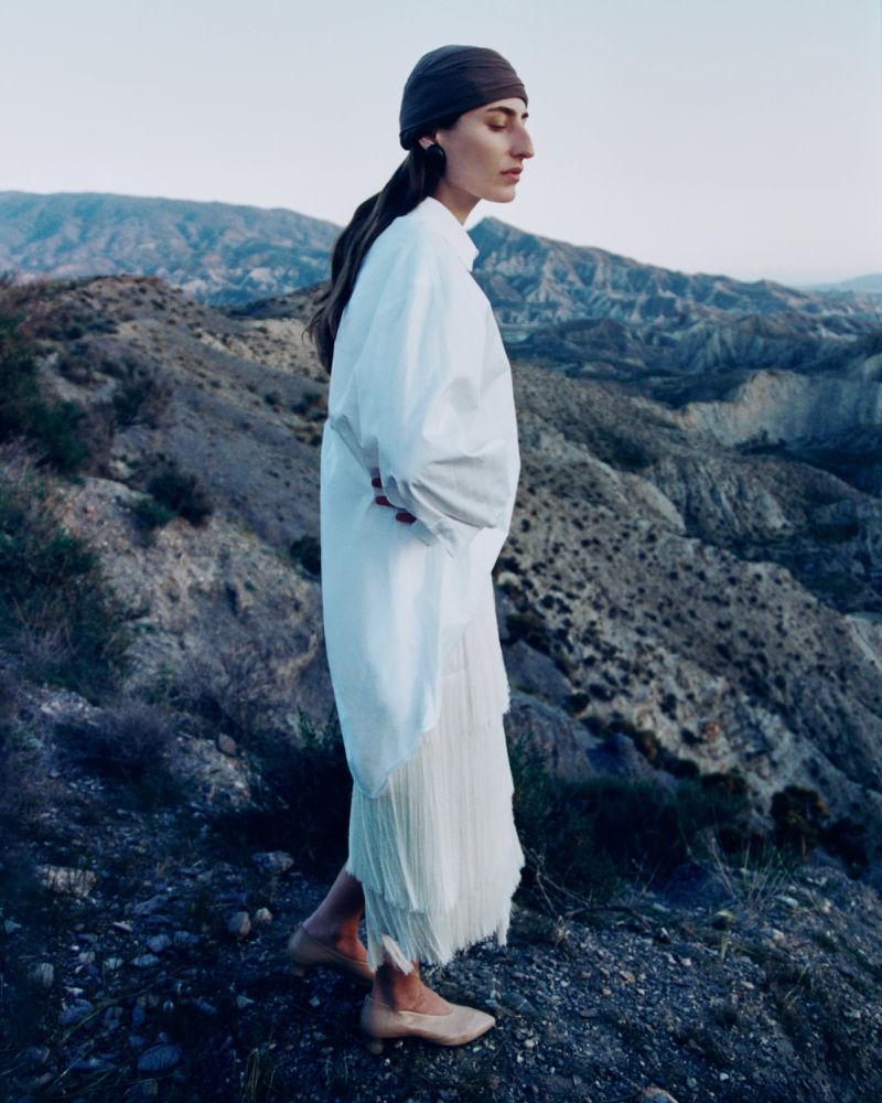 Woman wearing a white shirt and skirt standing on a rugged mountain terrain for Annabelle Magazine editorial