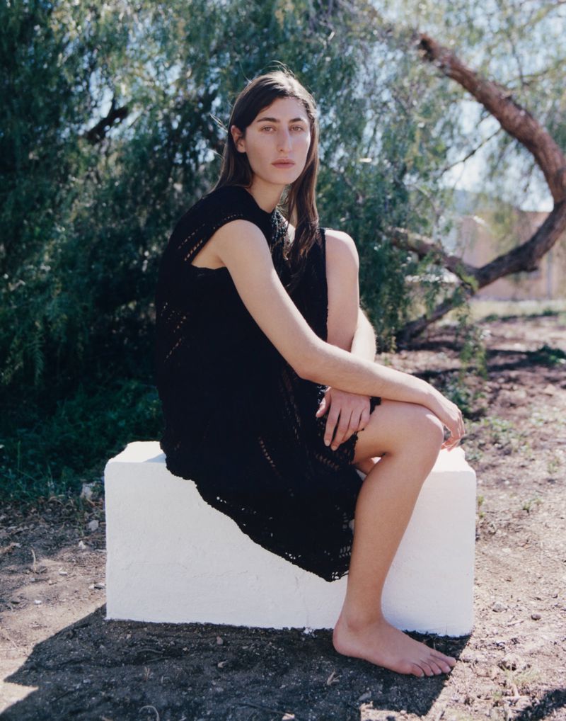 Woman in a black knitted dress sitting on a white block outdoors for Annabelle Magazine Nomadsland editorial