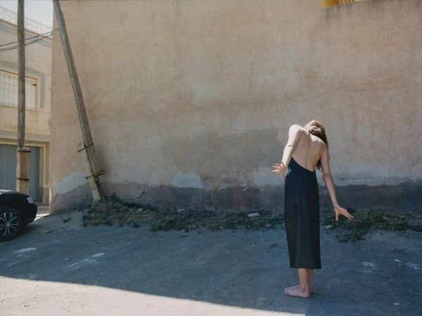 Woman in a black dress standing barefoot on pavement against a rustic stucco wall for Annabelle Magazine Nomadsland project.