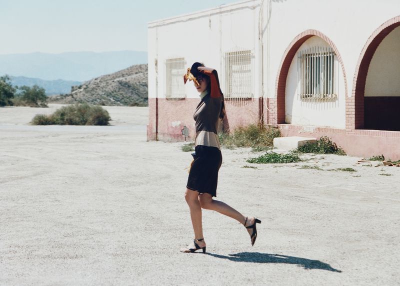 Model walking past a white and red building in an arid landscape for Nomadsland by Annabelle Magazine.