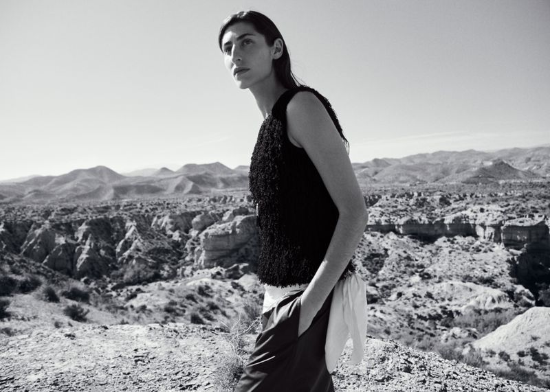 Model standing outdoors in a textured black top against an arid desert mountain landscape in a black and white fashion editorial.