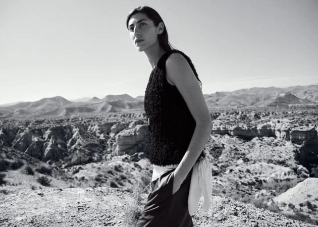 Model standing outdoors in a textured black top against an arid desert mountain landscape in a black and white fashion editorial.