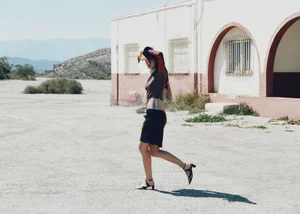 Model walking past a white and red building in an arid landscape for Nomadsland by Annabelle Magazine.