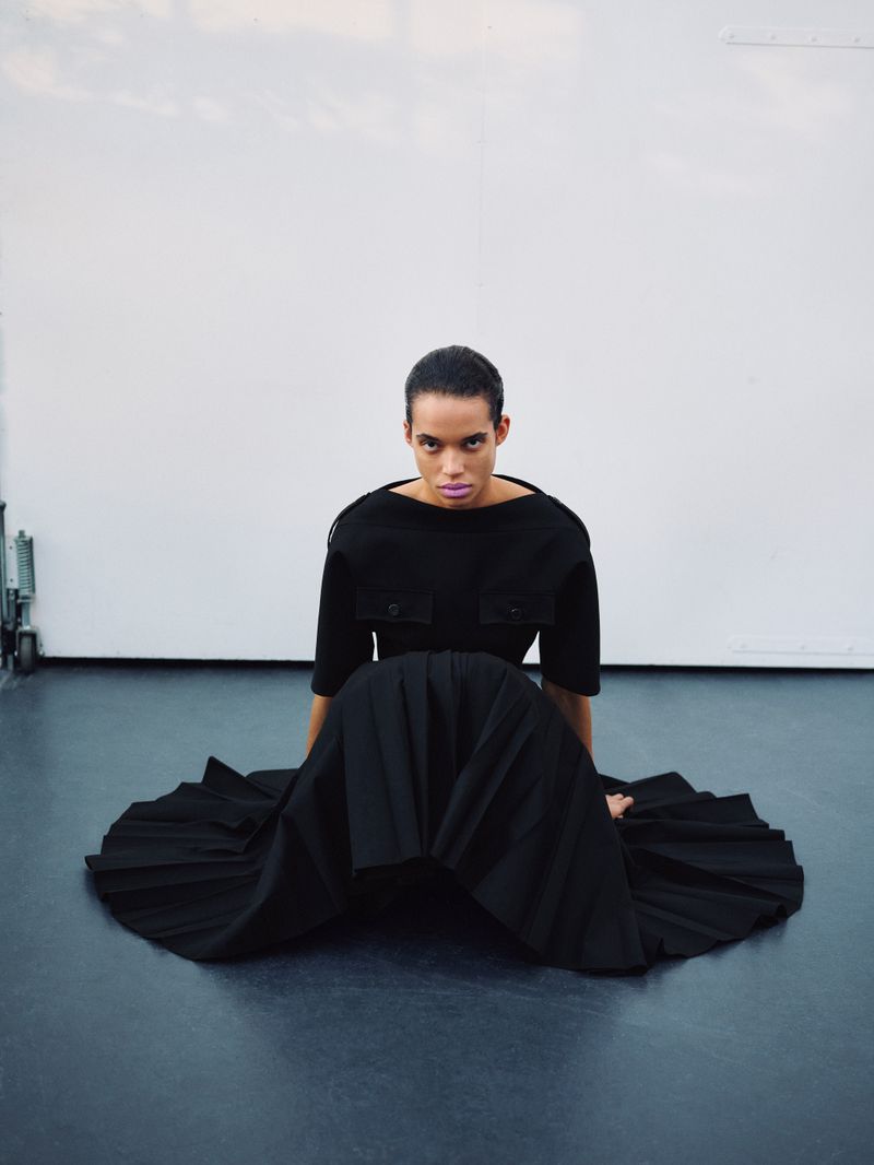 Model Lara Menezes seated on the floor in a black pleated skirt and top for Exit Magazine Black Orchid editorial