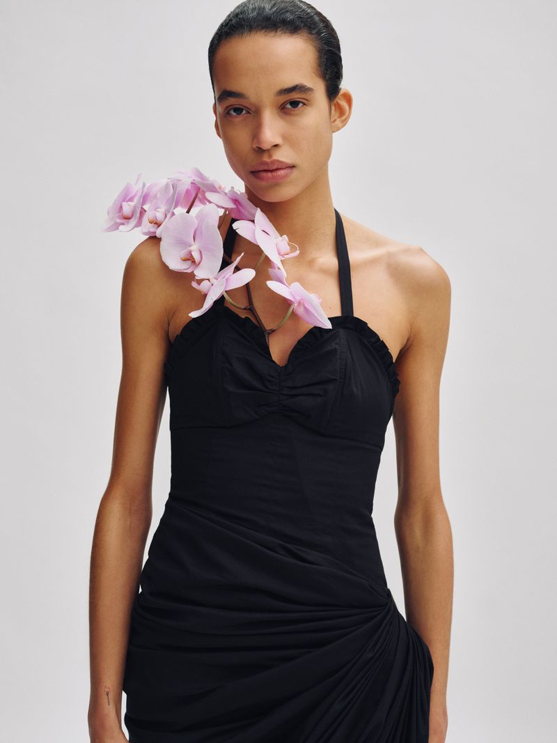 Model in a black halter dress with pink orchids draped over her shoulder against a neutral background