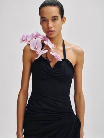 Model in a black halter dress with pink orchids draped over her shoulder against a neutral background