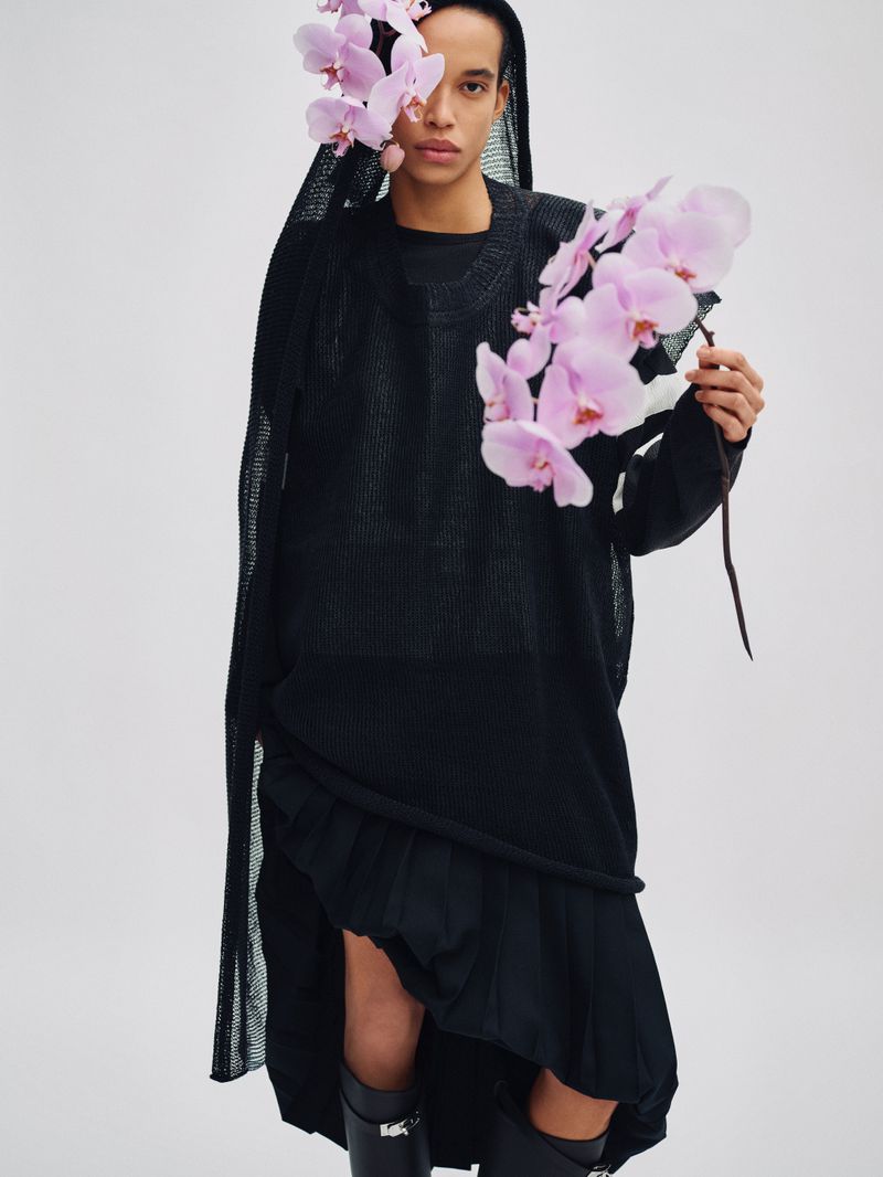 Model wearing a black mesh hooded top holding a branch of pink orchids for Exit Magazine Black Orchid project