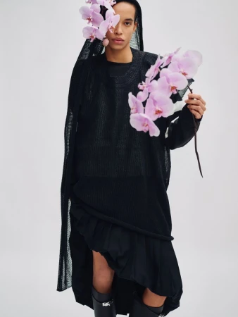 Model wearing a black mesh hooded top holding a branch of pink orchids for Exit Magazine Black Orchid project