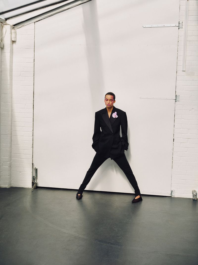 Model Lara Menezes wearing a black suit standing wide-legged against a large white warehouse door for Exit Magazine
