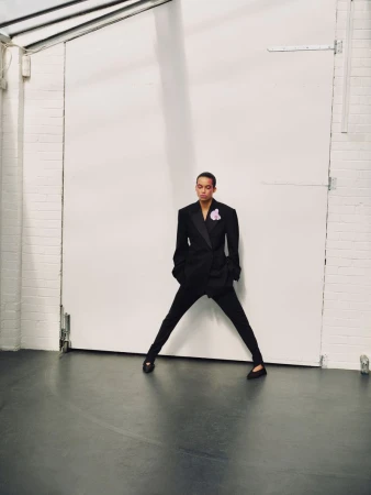 Model Lara Menezes wearing a black suit standing wide-legged against a large white warehouse door for Exit Magazine
